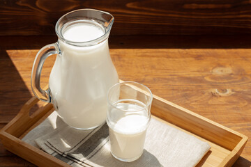 Glass pitcher of milk on old wooden table