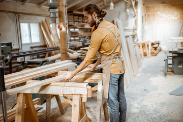 Naklejka na ściany i meble Handsome carpenter choosing planks for his woodwork at the joiners warehouse
