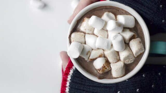 A Cup of cocoa with marshmallows and women's hands.
