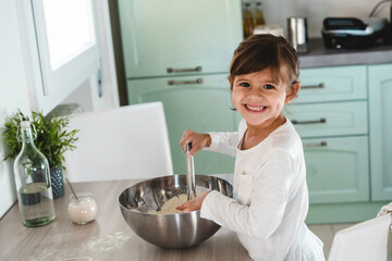 Obraz na płótnie Canvas Little cute girl is cooking on kitchen while smiling and looking at camera - Having fun while making pizza or bread dough - Childhood concept and having fun cooking - Copy space for text on left