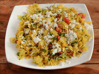 Dapde Pohe is a typical Maharashtrian breakfast, made with thin variety of poha and fresh coconut with chilli, peanuts and nuts. served in a plate over a rustic wooden background, selective focus