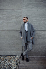 Full length body size photo of young businessman in grey coat scarf standing outside isolated on grey wall background