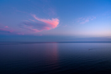 Sunset on the sea and a beautiful pink cloud against a blue sky.