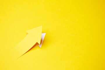 Right-up arrow cutted from solid sheet of yellow paper and curved up of one side with white paper underlay showing growth of stock market or up direction - obrazy, fototapety, plakaty