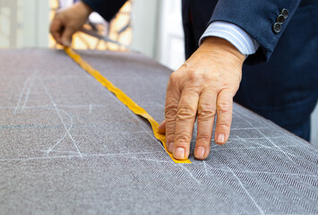 The hands of an elderly tailor preparing the pattern of the men's jacket to cut and sew it
