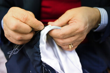 The hands of an elderly tailor basting and sewing the men's jacket. Sartorial clothes are made by...