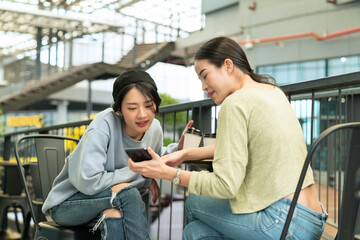 Two young woman having fun with smartphones at coffee breaks in public places. Business people using cellular mobile phone in a street cafe. 5G communication technology, internet networks concepts