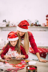 A young mother stands in the kitchen next to her daughter and watches as she prepares the dough.