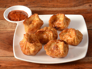 Chicken fried momo with sauce served over a rustic wooden background, selective focus