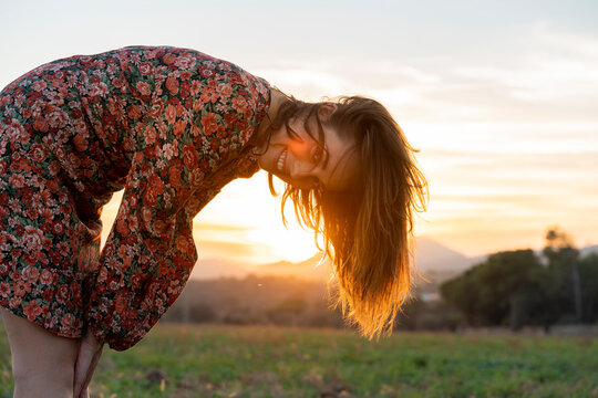 Smiling young woman with brown hair bending over during sunset