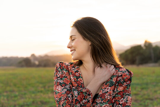 Happy woman embracing herself against sky during sunset