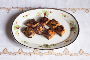 Some hake loins in butter with garlic and paprika on a decorated antique plate and a cloth tablecloth. Plating food.