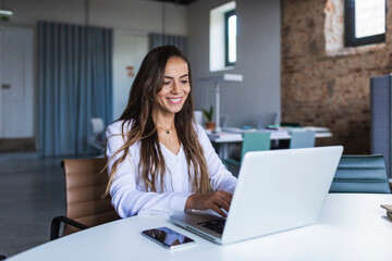 Cheerful businesswoman using laptop at desk in office