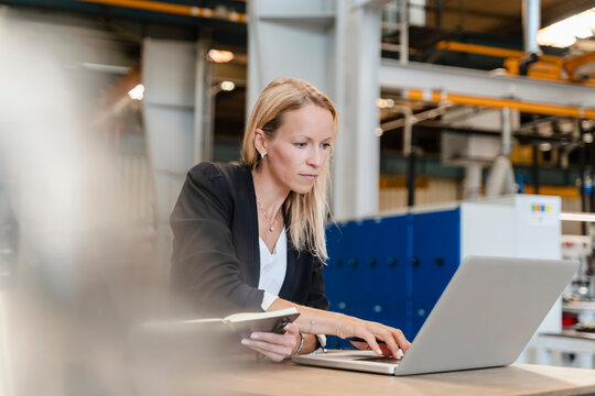 Female entrepreneur working on laptop while sitting in factory