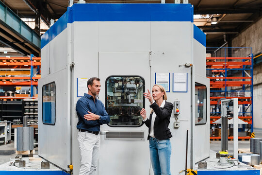 Female entrepreneur explaining male colleague while standing against control room in industry