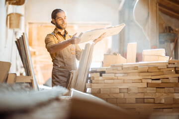 Carpenter or warehouse worker choosing raw wood material for the work at the sunny carpentry storage