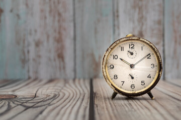 An old and stained alarm clock on a wooden background