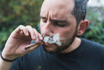 Handsome man smoking marijuana joint outdoors