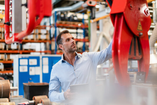 Businessman examining claw machine while holding digital tablet standing in factory