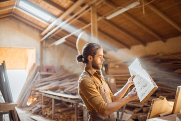 Carpenter or warehouse worker choosing raw wood material for the work at the sunny carpentry storage