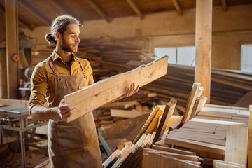 Carpenter or warehouse worker choosing raw wood material for the work at the sunny carpentry storage