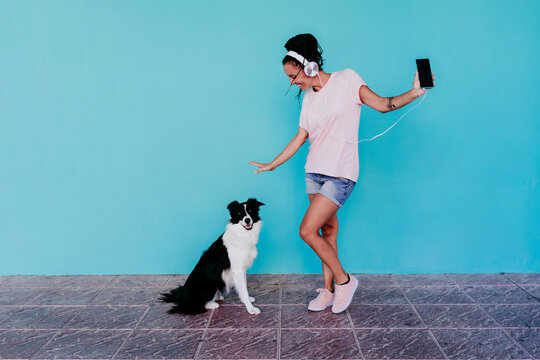 Happy woman listening music through headphones while dancing by Border Collie dog against turquoise wall