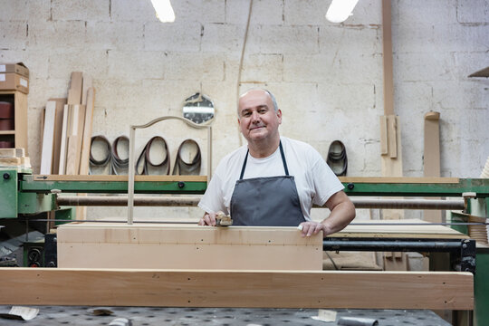 Smiling mature man holding plank while standing at workshop