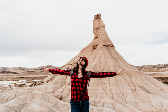 Spain, Navarre, Portrait of female tourist standing with raised arms in front of sandstone rock formation in Bardenas Reales