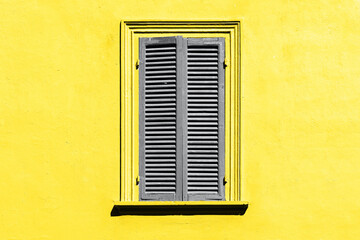 Trendy color of the year 2021. Ultimate grey and illuminating yellow. Gray shutters on the window against a yellow wall. Old window exterior in italian or greek village