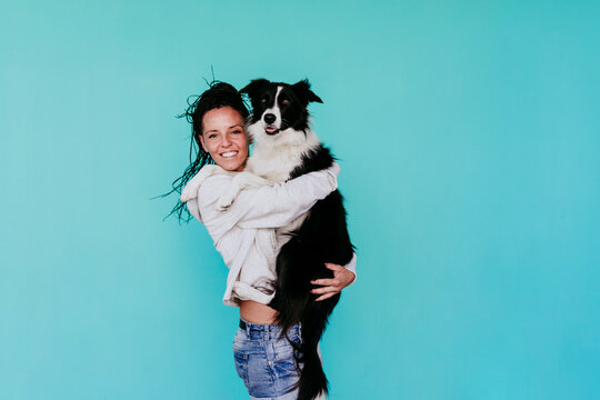 Happy woman carrying Border Collie dog against turquoise background