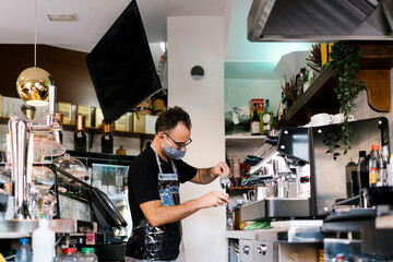 Male barista wearing protective face mask while working in cafe during COVID-19 crisis