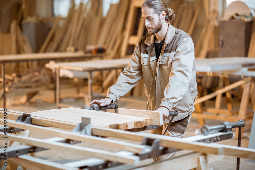 Wall mural Handsome carpenter in uniform gluing wooden bars with hand pressures at the carpentry manufacturing