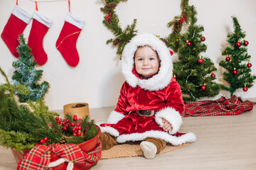 Little cute boy dressed as Santa near little Christmas trees. Christmas mood