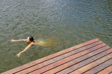 Young lady swimming in a small lake surrounded by green land and wood forest.. Monte Alegre Do Sul, Brazil. 