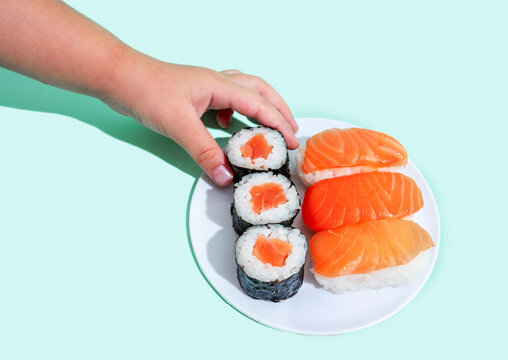 Hand of little girl picking up piece of maki sushi