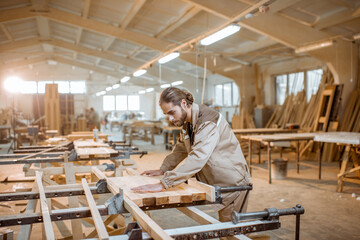 Handsome carpenter in uniform gluing wooden bars with hand pressures at the carpentry manufacturing - 398529982