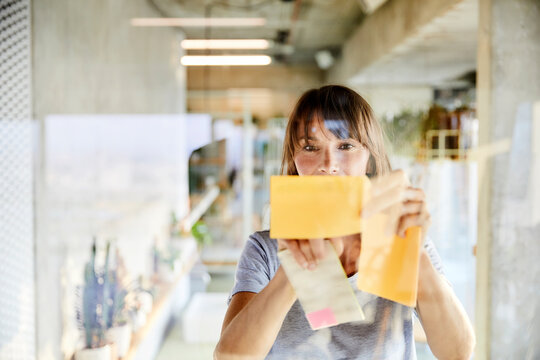 Mature woman sticking sticky notes on glass material