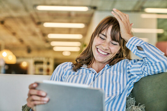 Woman with head in hand laughing while using digital tablet at home