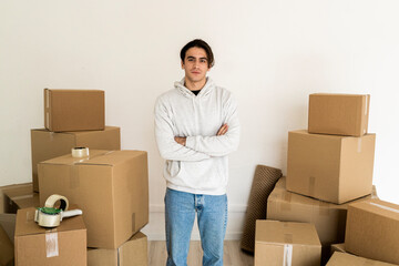 Young man with arms crossed standing amidst cardboard boxes in new house