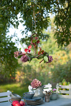 Lamp shade made of leaves and blooming hydrangeas hanging over coffee table set in garden