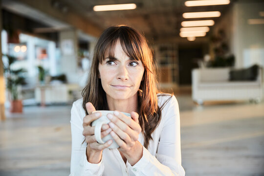 Mature Woman Looking Away While Drinking Coffee At Home