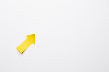 Right-up yellow paper arrow curved up of both sides which lies on the solid white paper background, showing growth of stock market or up direction