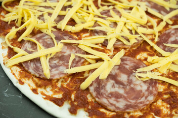 Pizza preparation. Raw dough with grated cheese and ingredients