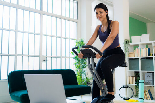 Young woman listening music through bluetooth while sitting on exercise bike at home
