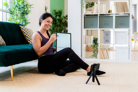 Female influencer showing graphics tablet while video recording on camera at home