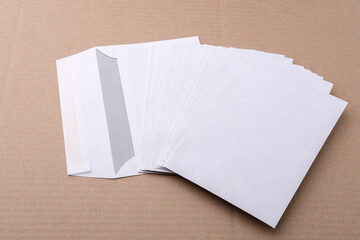 Mail white envelopes are scattered on the table. The packaging for paper letters and small parcels lies on corrugated cardboard. Stationery for delivery and logistics services.