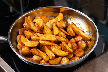 Sausages in sauce with potatoes on the pan on the stove.