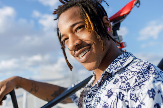 Smiling man looking away while carrying bicycle against sky