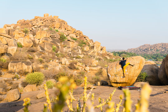 Rock climber getting on top of boulder lying at foot of rocky hill