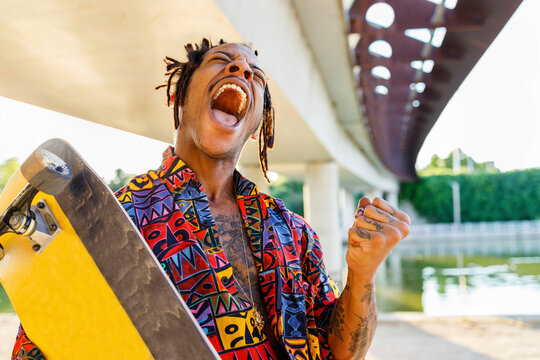 Young man with skateboard screaming while standing against bridge
